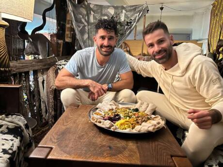 Seby and Stefan of Nomadic Boys smiling at the camera with a big plate of Ethiopan food from Madam Taitou.