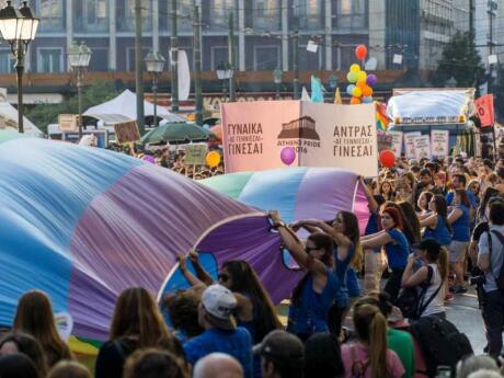 People marching in Athens Pride with a big rainbow flag.