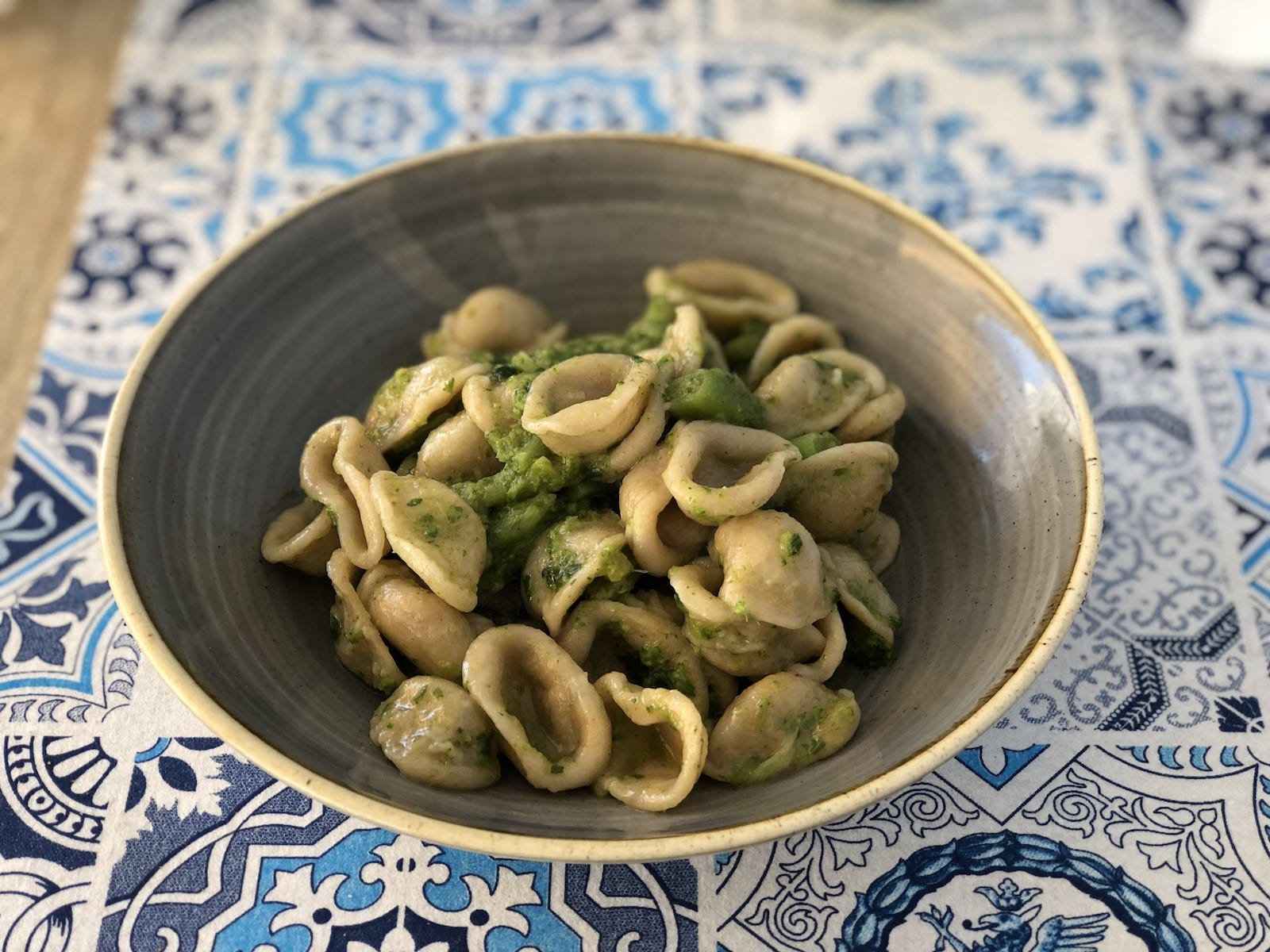 A bowl of shell-shaped pasta sitting on a table tiled in white and blue.